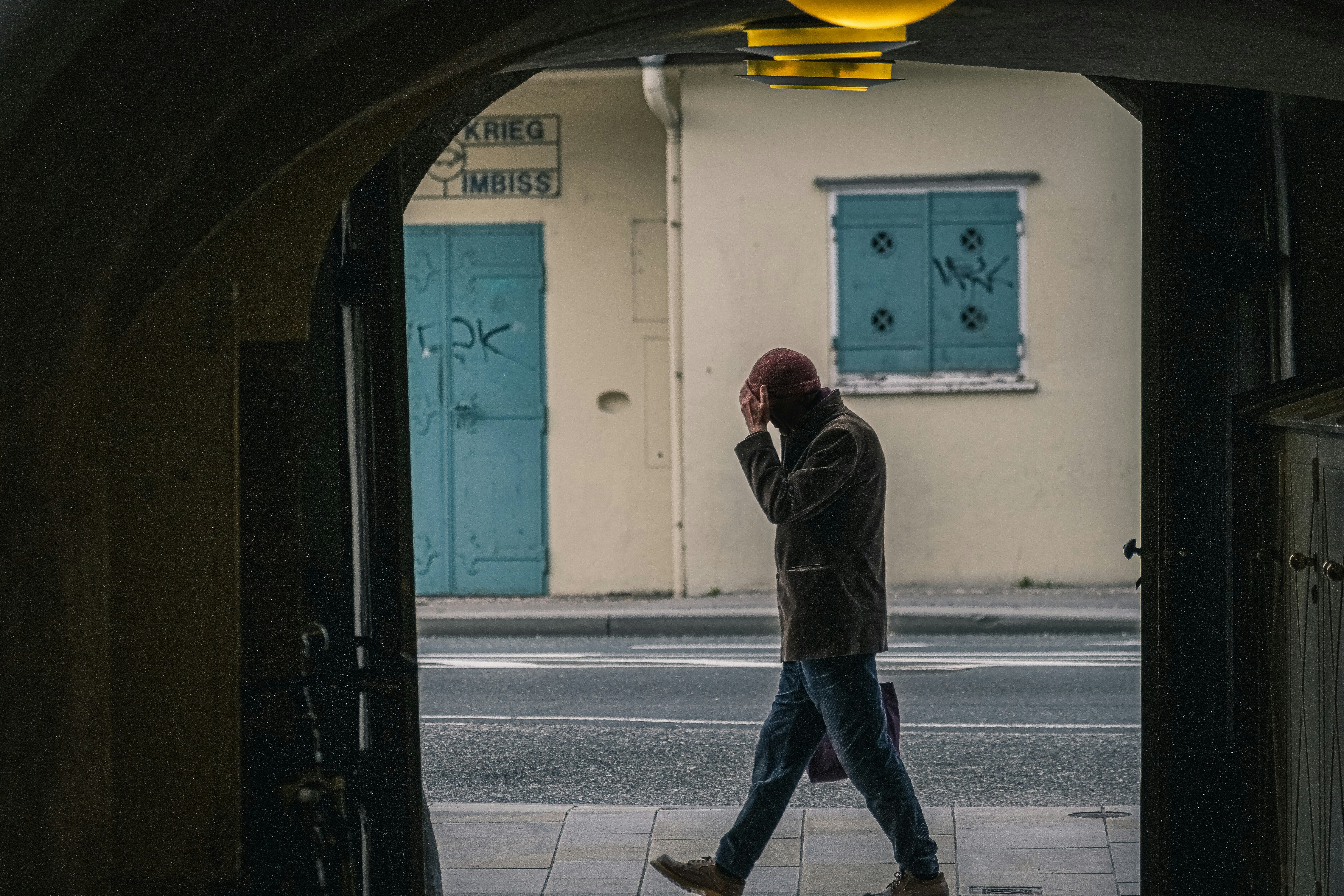 man in black jacket and blue denim jeans standing on sidewalk during daytime